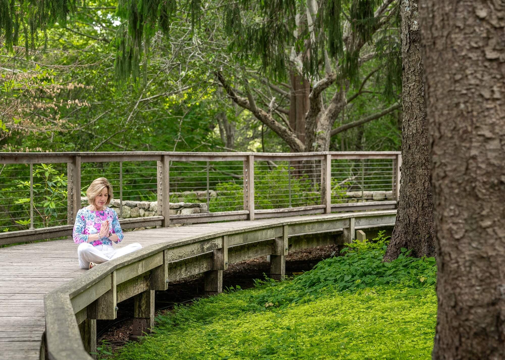 Lisa Parenteau meditating on a boardwalk among the trees